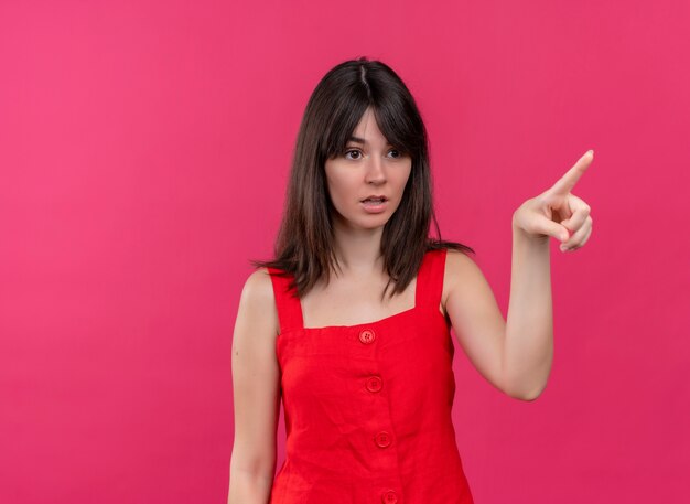 Chica caucásica joven sorprendida apunta hacia el lado sobre fondo rosa aislado con espacio de copia