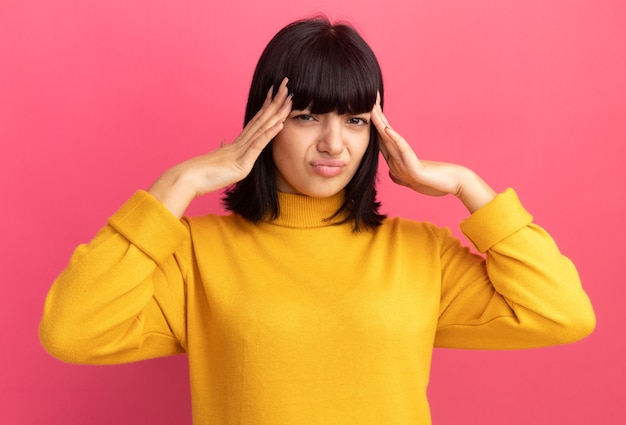 Chica caucásica morena joven molesta pone las manos en la cabeza en rosa