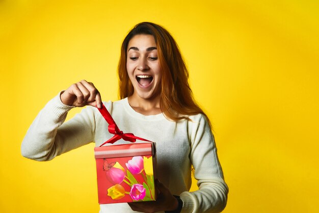 Chica caucásica pelirroja emocionada está abriendo presente con cara de sorpresa