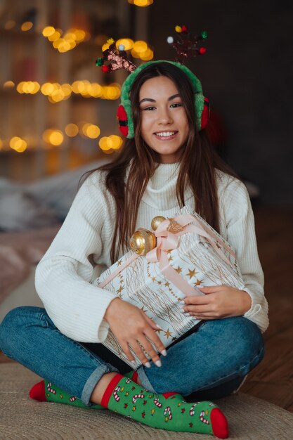 Chica de cerca con regalo sonriendo. Lleva cuernos de Navidad.