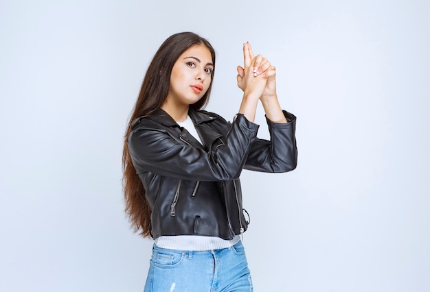 Chica con chaqueta de cuero mostrando signo de pistola en la mano.