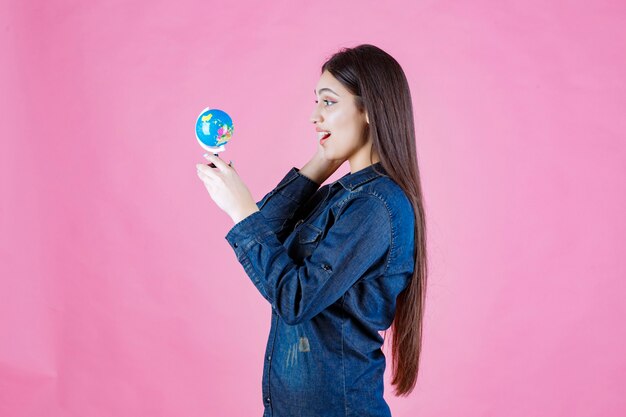 Chica en chaqueta de mezclilla sosteniendo un globo terráqueo y parece sorprendida