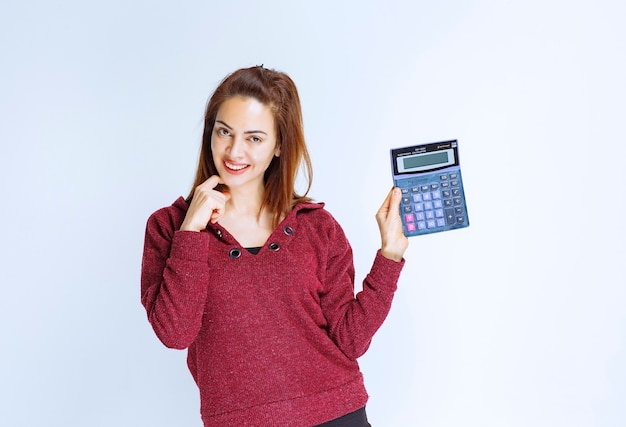 Chica de chaqueta roja calculando algo en una calculadora azul y demostrando el resultado final.