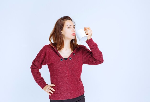 Chica de chaqueta roja sosteniendo una taza de café con leche.