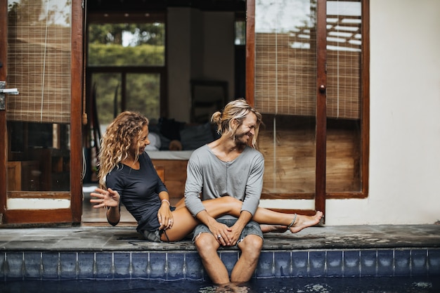 Chica y chico están sentados alrededor de la piscina, divirtiéndose y salpicando agua