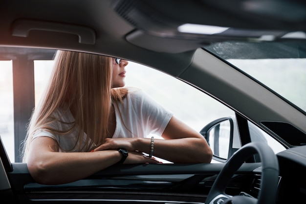 Chica y coche moderno en el salón. Durante el día en interiores. Comprar vehículo nuevo