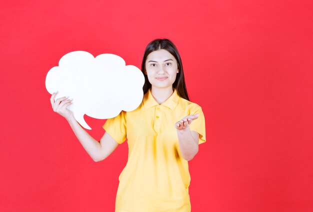 Chica en código de vestimenta amarillo sosteniendo un tablero de información en forma de nube e invitando a alguien a su lado