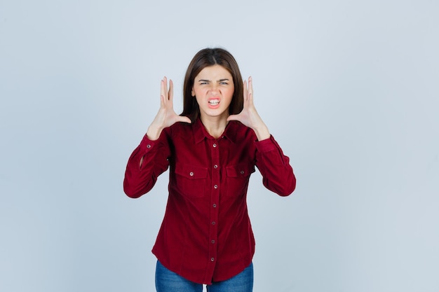 chica cogidos de la mano cerca de la cabeza con camisa burdeos y aspecto agresivo.