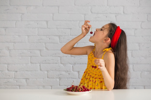 Chica comiendo alegre fresco rojo delante de la pared de ladrillo