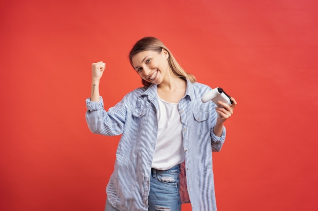 La chica competitiva celebra el controlador de joystick de juego de explotación ganador en la pared roja.