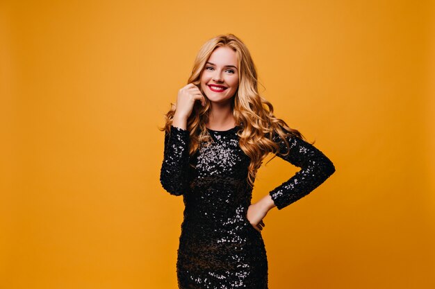 Chica complacida en vestido de moda preparándose para la fiesta. Adorable mujer guapa posando en la pared amarilla.