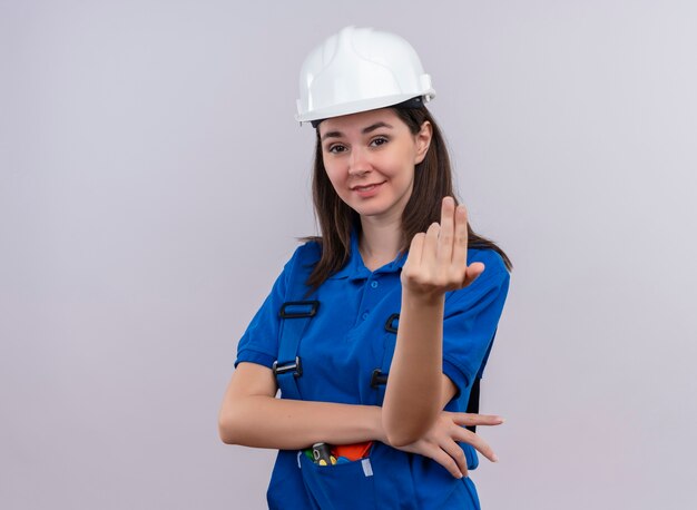 Chica constructora joven confiada con casco de seguridad blanco y uniforme azul finge llamar a alguien sobre fondo blanco aislado con espacio de copia