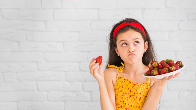 Chica contenta sosteniendo un plato de fresas rojas