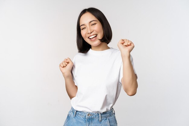 Chica coreana bailando feliz posando sobre fondo blanco con camiseta