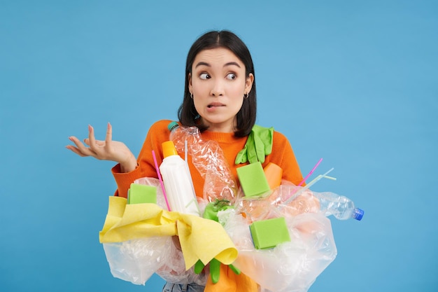 Foto gratuita chica coreana con basura plástica se encoge de hombros no sabe cómo reciclar clasificando sus residuos para r