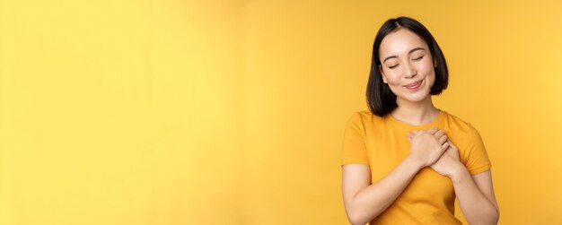 Chica coreana romántica mujer asiática cogidos de la mano en el corazón sonriendo con cuidado y ternura de pie ov