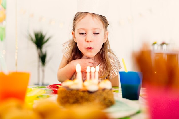 Chica en corona de papel soplando velas