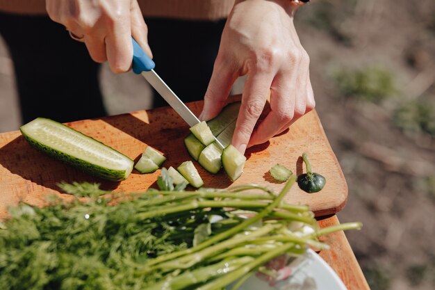 Chica corta verduras en el tablero y prepara una ensalada en la naturaleza exterior