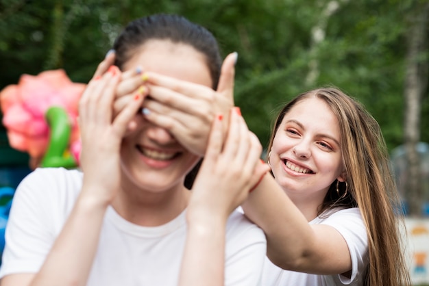 Chica cubriendo los ojos de su amiga en el parque de diversiones