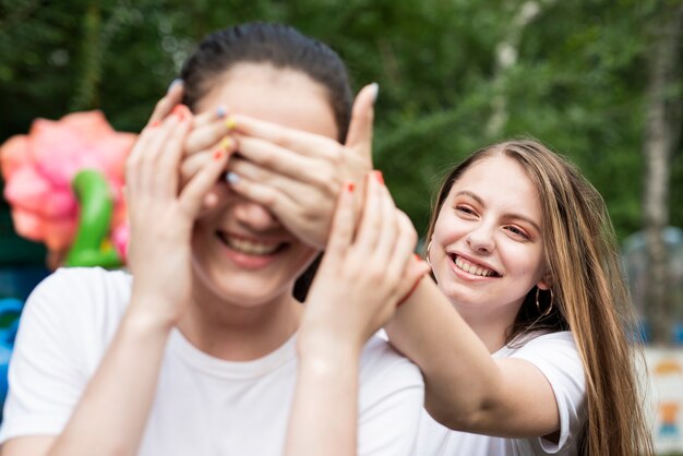 Chica cubriendo los ojos de su amiga en el parque de diversiones