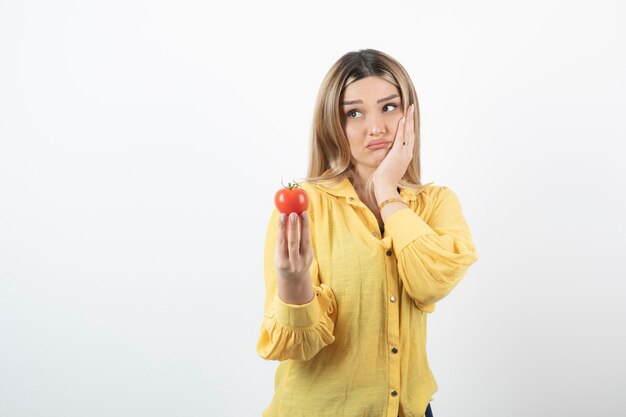 Chica decepcionada sosteniendo tomate rojo sobre blanco.