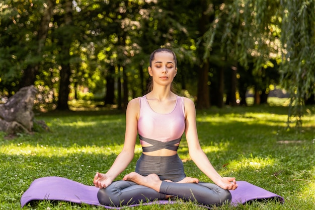 Chica delgada meditando sentado en una postura de loto con los ojos cerrados en el césped en un parque