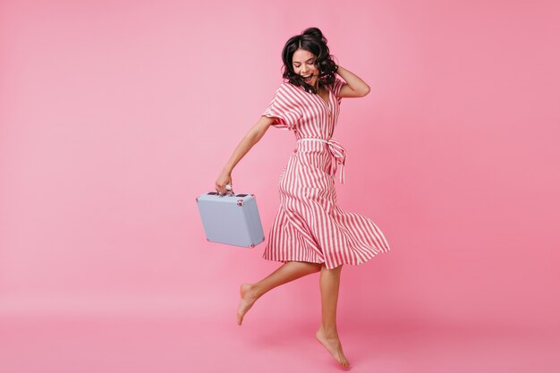 Chica delgada de muy buen humor se divierte y baila con el bolso en sus manos. Foto de modelo italiana con vestido cruzado.