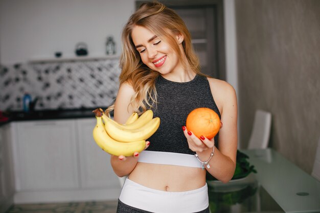 Chica de deportes en una cocina con frutas.