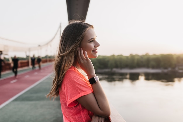 Foto gratuita chica deportiva alegre posando en la naturaleza borrosa. foto exterior de refinada mujer rubia disfrutando de vistas a la ciudad.