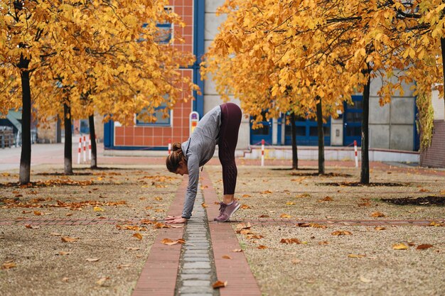 Chica deportiva atractiva que se extiende durante el entrenamiento en la calle de la ciudad de otoño