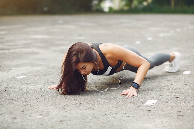 Chica deportiva entrenando con auriculares en un parque de verano