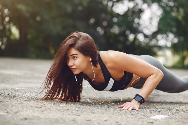 Chica deportiva entrenando con auriculares en un parque de verano