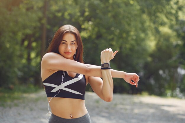 Chica deportiva entrenando con auriculares en un parque de verano