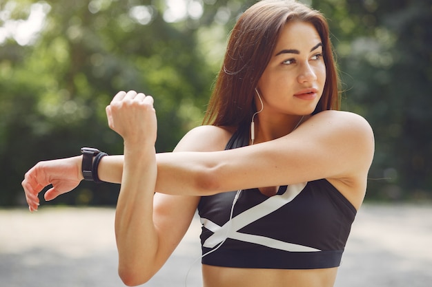 Chica deportiva entrenando con auriculares en un parque de verano