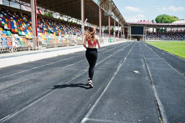 Chica deportiva fitness en ropa deportiva en el estadio deportes al aire libre Mujer sexy feliz corriendo en la cinta de correr de la pista atlética en el estadio