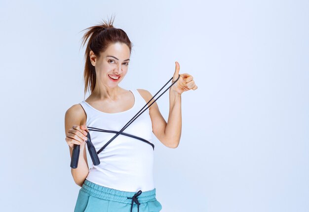 Chica deportiva sosteniendo una cuerda de saltar azul y mostrando el pulgar hacia arriba.