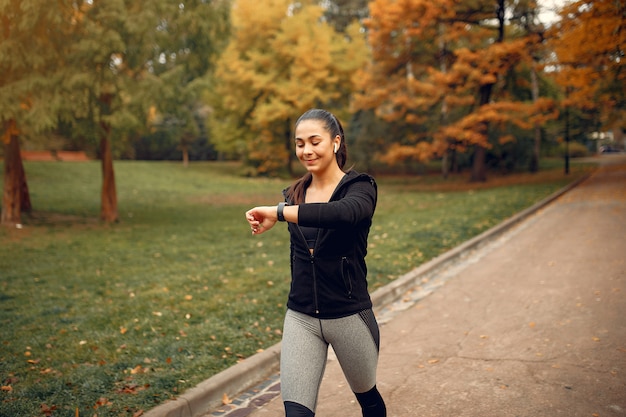 Chica deportiva en un top negro entrenamiento en un parque de otoño