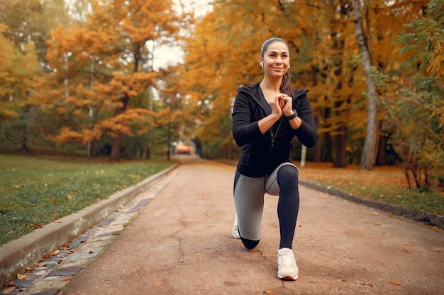 Chica deportiva en un top negro entrenamiento en un parque de otoño