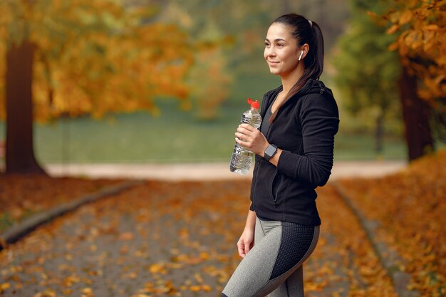 Chica deportiva en un top negro entrenamiento en un parque de otoño