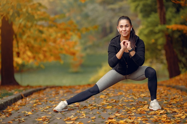 Chica deportiva en un top negro entrenamiento en un parque de otoño