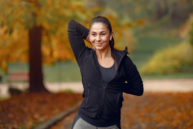 Chica deportiva en un top negro entrenamiento en un parque de otoño