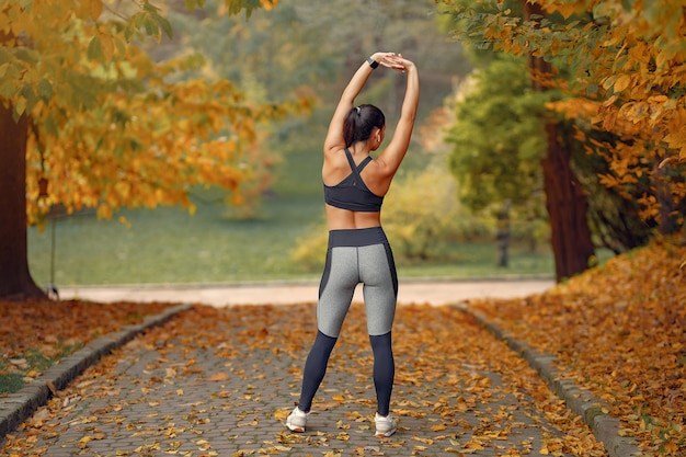 Chica deportiva en un top negro entrenamiento en un parque de otoño