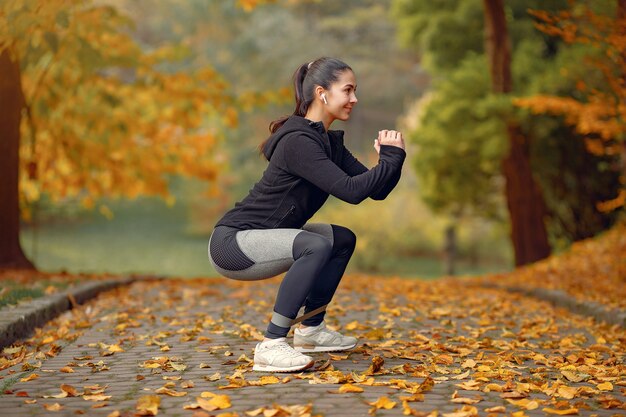 Chica deportiva en un top negro entrenamiento en un parque de otoño