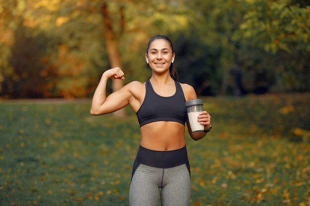 Chica deportiva en un top negro entrenamiento en un parque de otoño