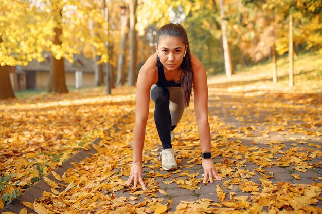 Chica deportiva en un top negro entrenamiento en un parque de otoño