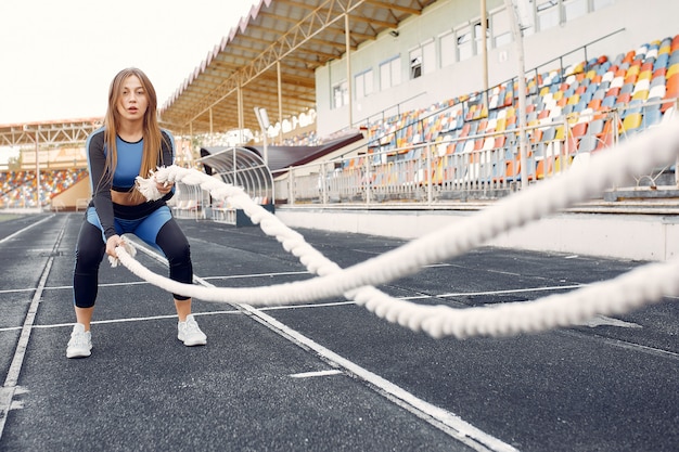 Chica deportiva en un uniforme azul entrenando en el estadio con una cuerda