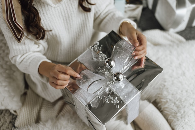 Foto gratuita chica está desempacando un regalo en papel plateado y cinta