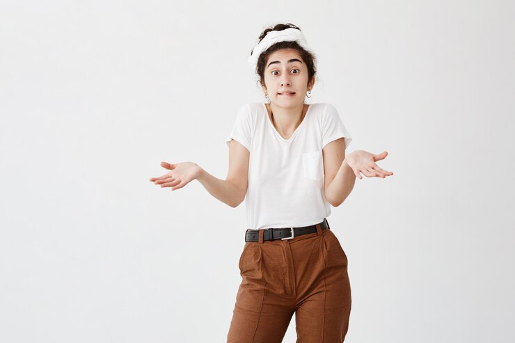Foto gratuito chica despistada con cabello oscuro en nudos gestos de perplejidad ya que no sabe la respuesta a una pregunta discutible. la joven modelo vacilante se encoge de hombros con desconcierto. concepto de lenguaje corporal