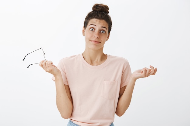 Foto gratuita chica despistada con gafas posando contra la pared blanca