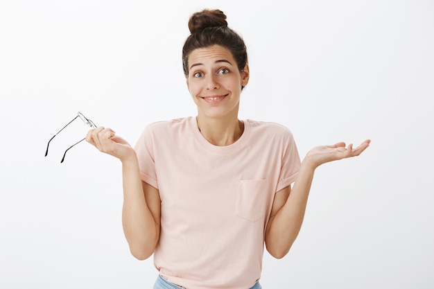 Chica despistada con gafas posando contra la pared blanca